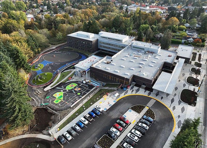 aerial view of a large L-shaped building with planters in front and a parking area with cars in it